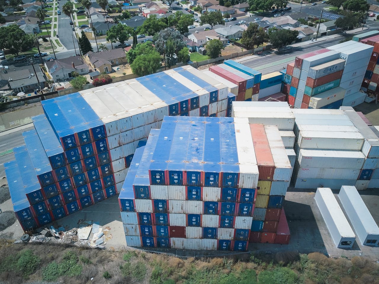 Drone shot of cargo containers stacked by residential houses, showing urban storage.